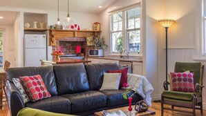 A modern kitchen with a brick fireplace, wooden shelves, and a dining area with a black leather sofa and a green armchair. - Lucy's Cottage in beautiful Kyneton (Kyneton)