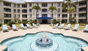 A hotel with a swimming pool, lounge chairs, and palm trees.