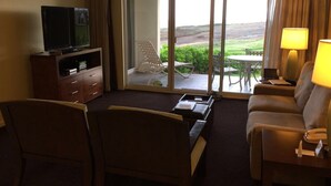 Ein Hotelzimmer mit Fernseher, Sofa, Sessel, Schreibtisch und Blick ins Freie.