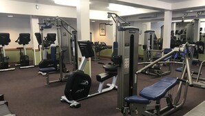 Ein Fitnessstudio mit verschiedenen Trainingsgeräten, darunter Laufbänder, Kraftgeräte und eine Hantelbank.