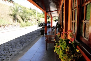 Un espacio al aire libre cubierto, con suelo de piedra, bancos de madera y plantas en macetas.