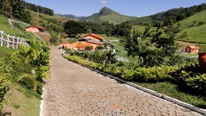 Un sendero adoquinado que conduce a un edificio con techo rojo, rodeado de exuberante vegetación y colinas al fondo.