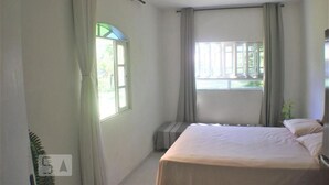 A bedroom with a bed, a window with curtains, and a radiator. - Casa Pátio Grande / 8 people - Praia do Moçambique (Florianópolis)