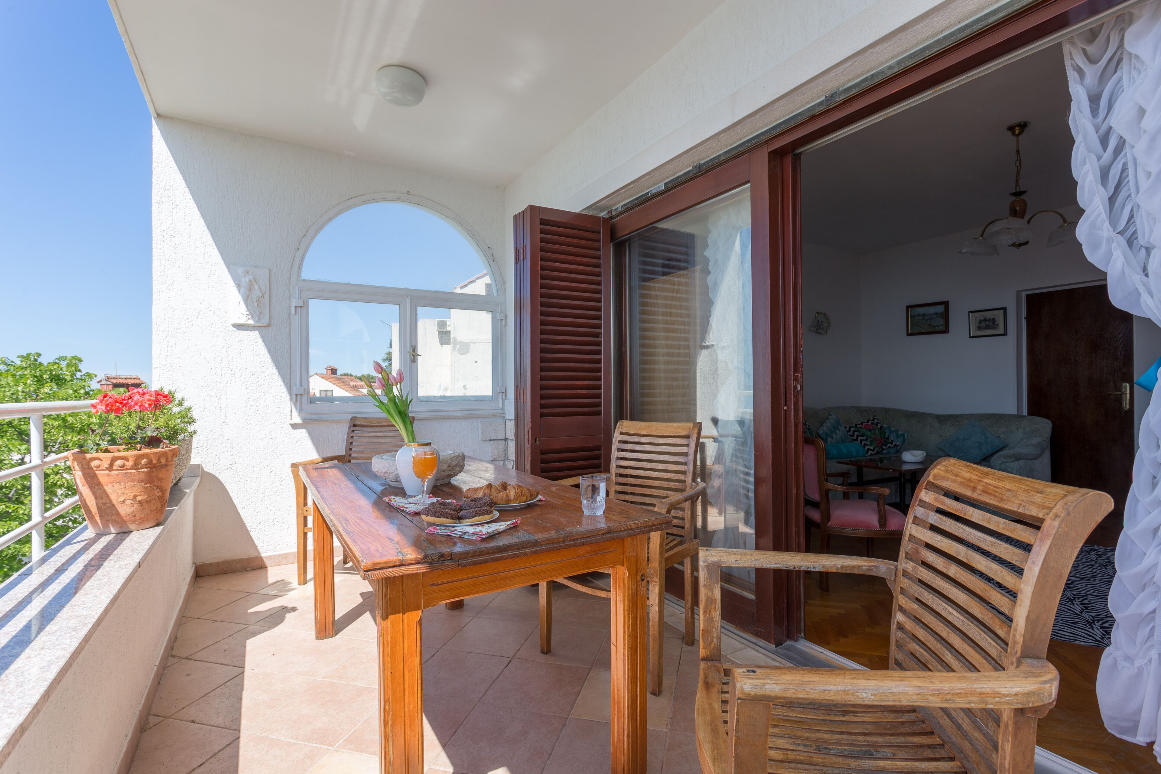 Ein Balkon mit Holztisch und -stühlen, einem Blumentopf und Blick ins Innere.