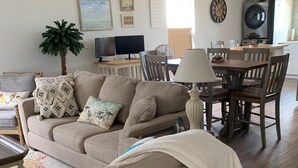 A living room with a beige sofa, a dining table with chairs, a lamp, a television, and a clock on the wall. - Beachfront Home with Outstanding Beach Views; Quick Walk to Ocean. (Matagorda)