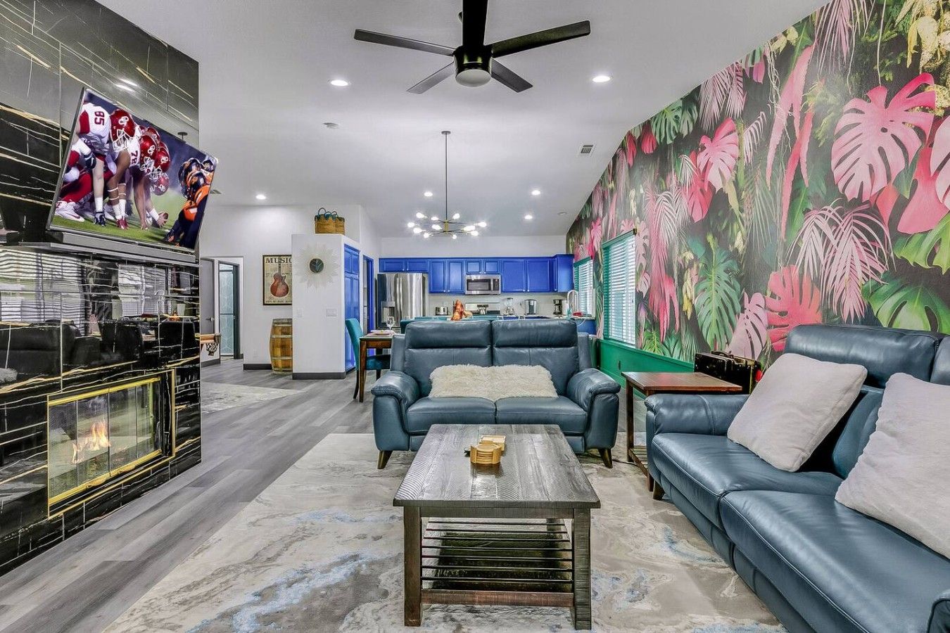 A living room with a fireplace, a blue sofa set, a coffee table, and a large tropical-themed mural.