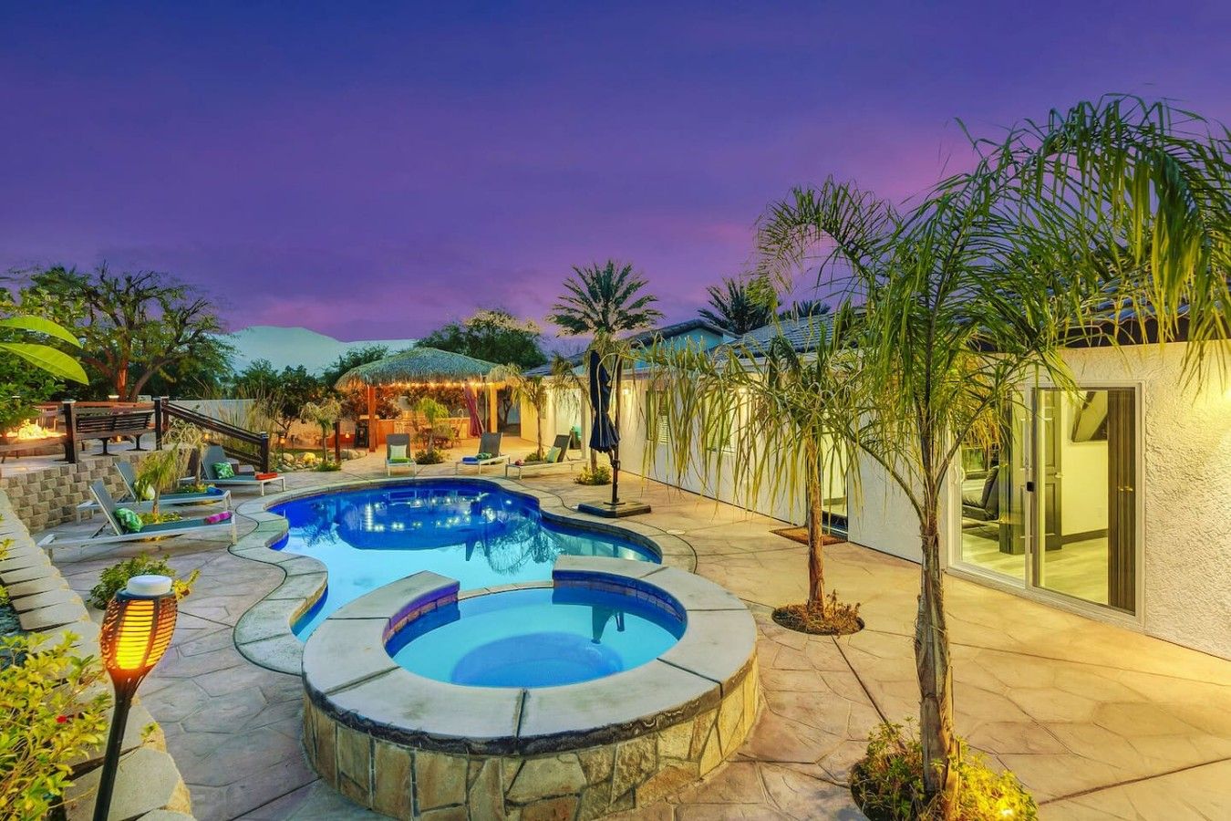 A pool area with a hot tub, lounge chairs, and a covered seating area.