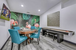 A room with a pool table, a dining table with chairs, and a wall with a flamingo mural. - Casa Del Sol: #259070 Pool, Spa, Game Room, Court (La Quinta)
