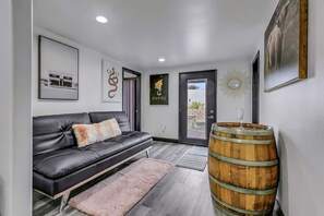 A modern living room with a leather sofa, a wooden barrel, and framed artwork on the walls. - Casa Del Sol: #259070 Pool, Spa, Game Room, Court (La Quinta)