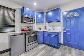 A compact kitchen with blue cabinets, a stainless steel refrigerator, a gas stove, a microwave, and a sink. - Casa Del Sol: #259070 Pool, Spa, Game Room, Court (La Quinta)