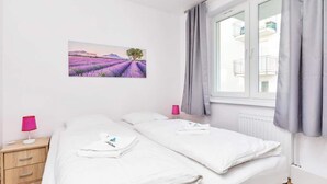 Una camera da letto con un letto, un comodino, una lampada, una finestra con tende e un quadro di campi di lavanda.