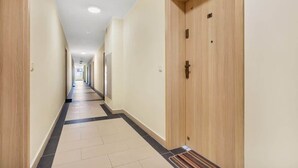 Un lungo e stretto corridoio di un hotel, con porte in legno e pavimento piastrellato.