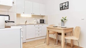 Una cucina funzionale con mobili bianchi, forno a microonde, bollitore e tavolo con sedie.