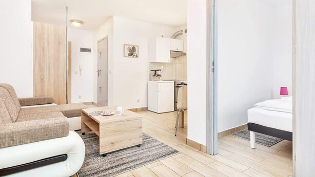 Un ambiente moderno e compatto con divano, un piccolo tavolo di legno, un letto, angolo cottura e bagno separato.