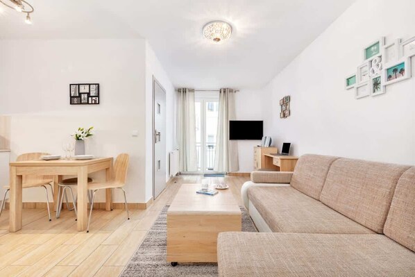 Un salon moderne comprenant un canapé, une table à manger avec des chaises, un téléviseur à écran plat et une petite table d’appoint.