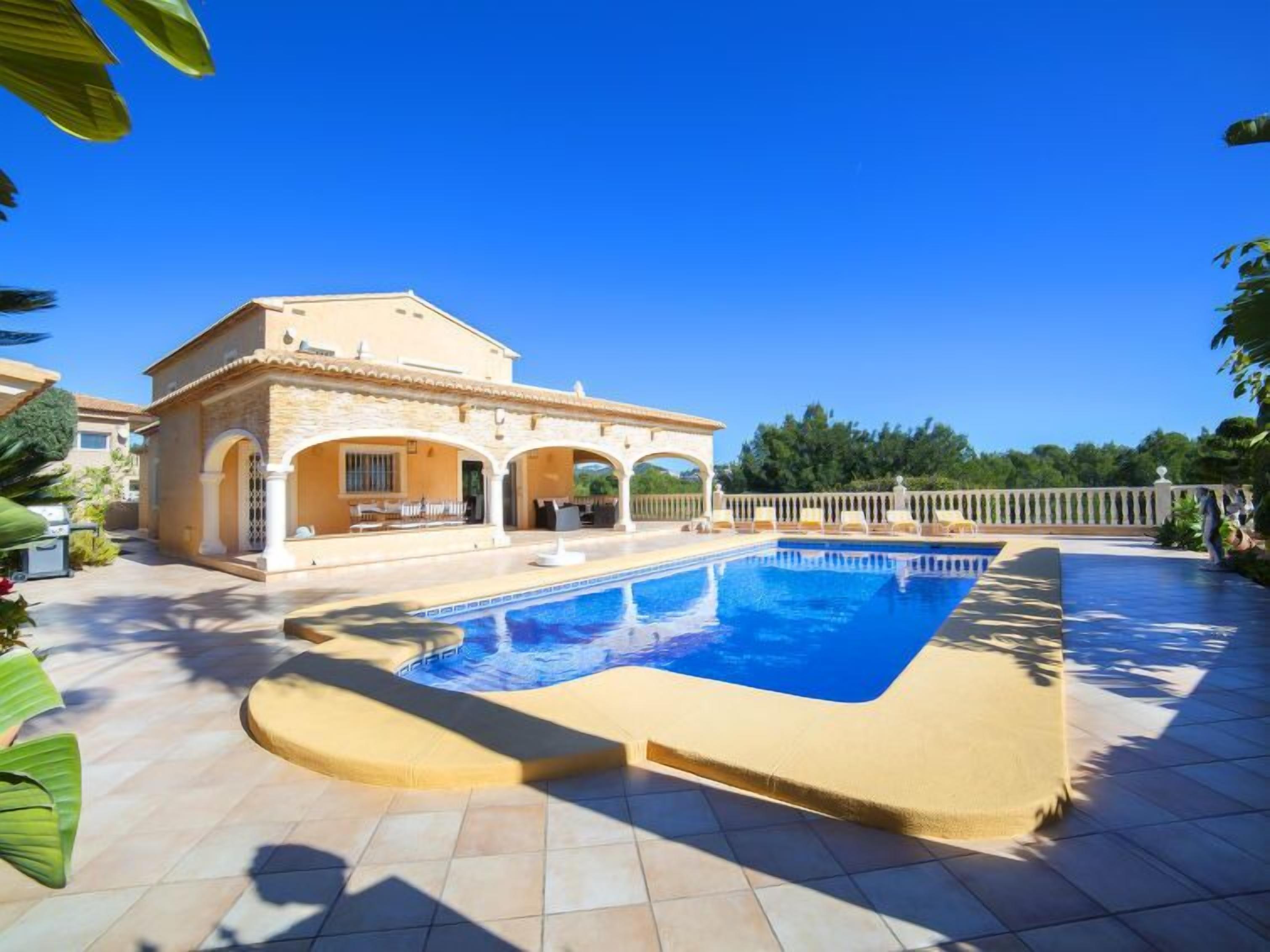 A poolside area with a pool, a covered patio, and a house with arches.