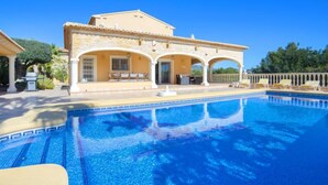 A poolside view of a Mediterranean-style building with a tiled pool, outdoor seating, and a clear blue sky. - Del Pozo by Interhome (Calpe/Calp)