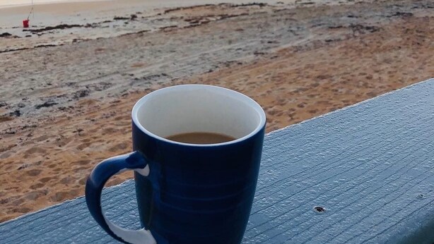 Una tazza blu su un molo di legno con vista su una spiaggia al tramonto.