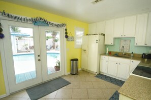 Una cocina con armarios blancos, un refrigerador y una ventana con vista a un patio trasero.