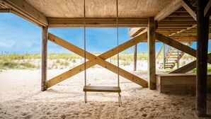 A wooden structure with a swing set in a sandy area, wooden beams, and a staircase leading to a higher level. - Salty But Sweet: Renovated Oceanfront Home on Oak Island with Great Views (Oak Island)
