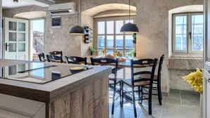 Une cuisine moderne dotée d’un îlot central, de luminaires suspendus et de grandes fenêtres offrant une vue sur l’extérieur.