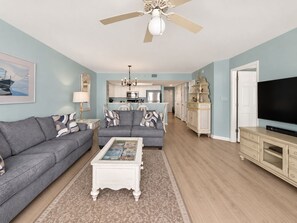 A living room with a grey sofa, a coffee table, and a television. - Coastal Calm | 316 COV |  Oceanfront Villa With Pool & Views (Folly Beach)