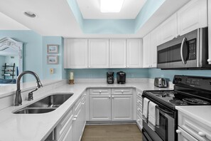 A kitchen with white cabinets, a stainless steel sink, a microwave, a stove, and a coffee maker. - Coastal Calm | 316 COV |  Oceanfront Villa With Pool & Views (Folly Beach)
