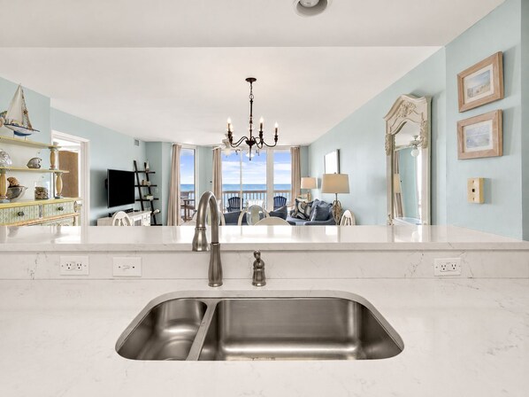 A modern kitchen with a large island, stainless steel sink, and a view to the outside.