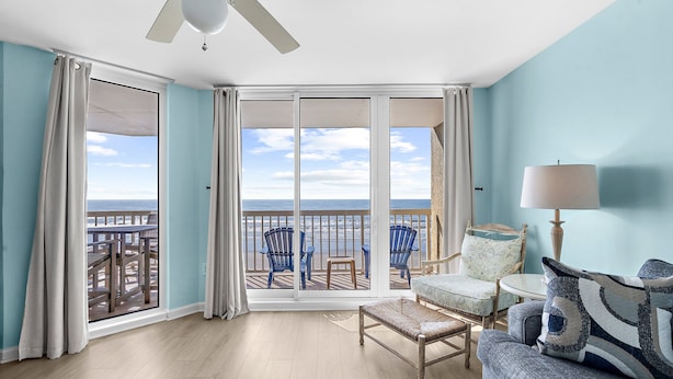 A room with a balcony, a ceiling fan, a sofa, and a chair.