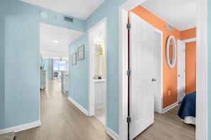 A hallway with a light blue wall, a white door, and a bed with a blue blanket. - Coastal Calm | 316 COV |  Oceanfront Villa With Pool & Views (Folly Beach)