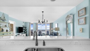 A modern kitchen with a large island, a chandelier, and a view to the outside.