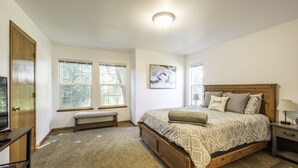 Een slaapkamer met een groot bed, een bankje, een televisie en een raam.