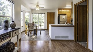 Een moderne keuken met houten kastjes, een eethoek met tafel en stoelen, en een groot raam dat voor natuurlijk licht zorgt.