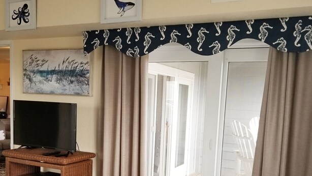 Un dormitorio con cama, un televisor sobre un mueble de madera, una ventana con cortinas y vistas a una terraza exterior.