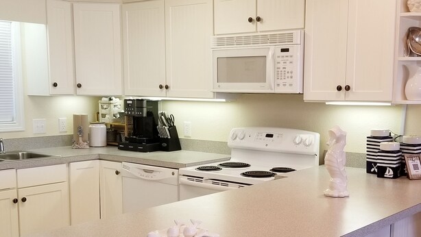Una cocina con armarios blancos, microondas, estufa y cafetera.