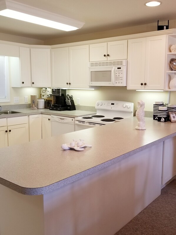 A kitchen with white cabinets, a microwave, a stove, and a coffee maker. - OCEAN/SOUND VIEW!OCEAN BOARDWALK!  BEACH EQUIP! BABY EQUIP! GUEST FAVORITE! (Rodanthe)