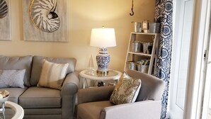 Un salón con un sofá gris, un sillón gris, un tapete estampado, una lámpara y decoración en la pared.