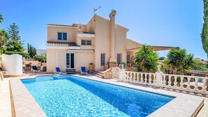 Una piscina con bordo piastrellato, un edificio con balcone e un recinto bianco.