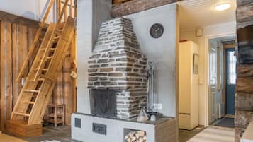Une cheminée en pierre avec une échelle en bois, une table blanche et une porte donnant sur une autre pièce.