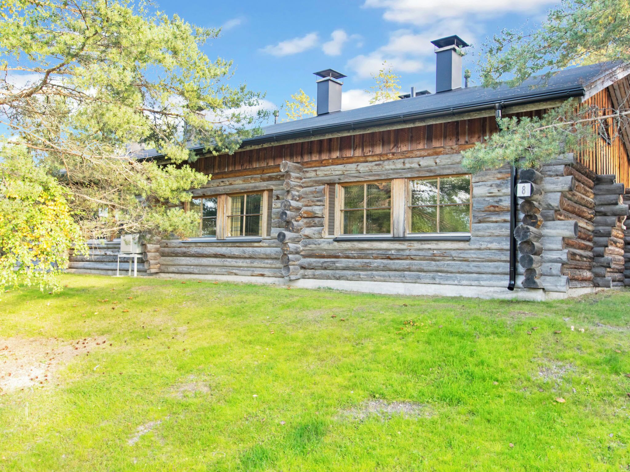 A log cabin with a stone foundation, large windows, and a chimney.