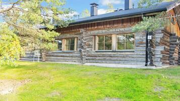 A log cabin with a stone foundation, large windows, and a chimney.
