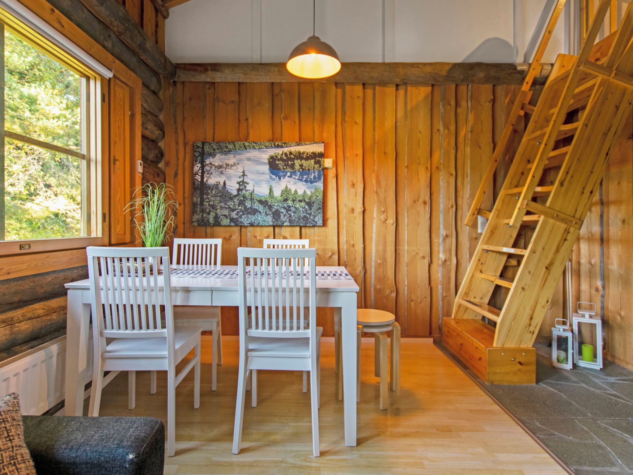 A wooden interior with a dining table, chairs, a painting, a plant, and a fireplace.