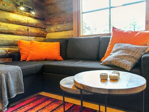 Interior acogedor de una cabaña de madera con un sofá seccional, una mesita redonda y un ventanal con vistas a árboles.