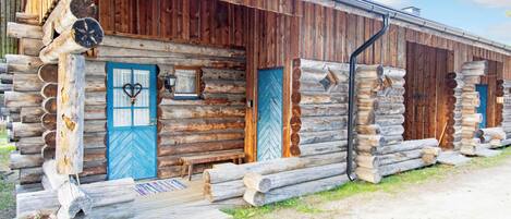 Una cabaña de troncos con puerta azul, un porche pequeño y una ventana.