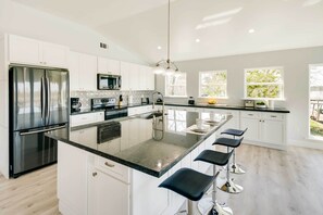 A modern kitchen with a central island, stainless steel appliances, white cabinetry, and bar stools. - Spacious San Jacinto River Home w/ Waterfront Deck (Houston)