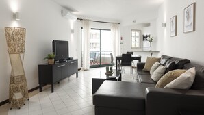 Una sala de estar moderna con un sofá negro, un televisor de pantalla plana y una zona de comedor con una mesa y sillas.