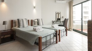 Habitación de hotel con dos camas, un escritorio, una silla y un balcón con vistas.