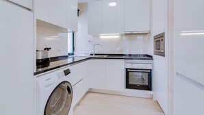 A modern kitchen with white cabinets, a built-in washing machine, a microwave, and an oven. - Taalia I - Vilamoura (Vilamoura)