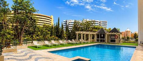 Una piscina con una solana empavedada, sillas de descanso y un pabellón.