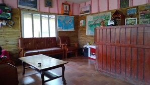 A room with a wooden floor, a brown leather sofa, a wooden table, and a red cabinet. There are framed pictures on the walls and a map on the wall. - Hotel Tress House (Sauraha)